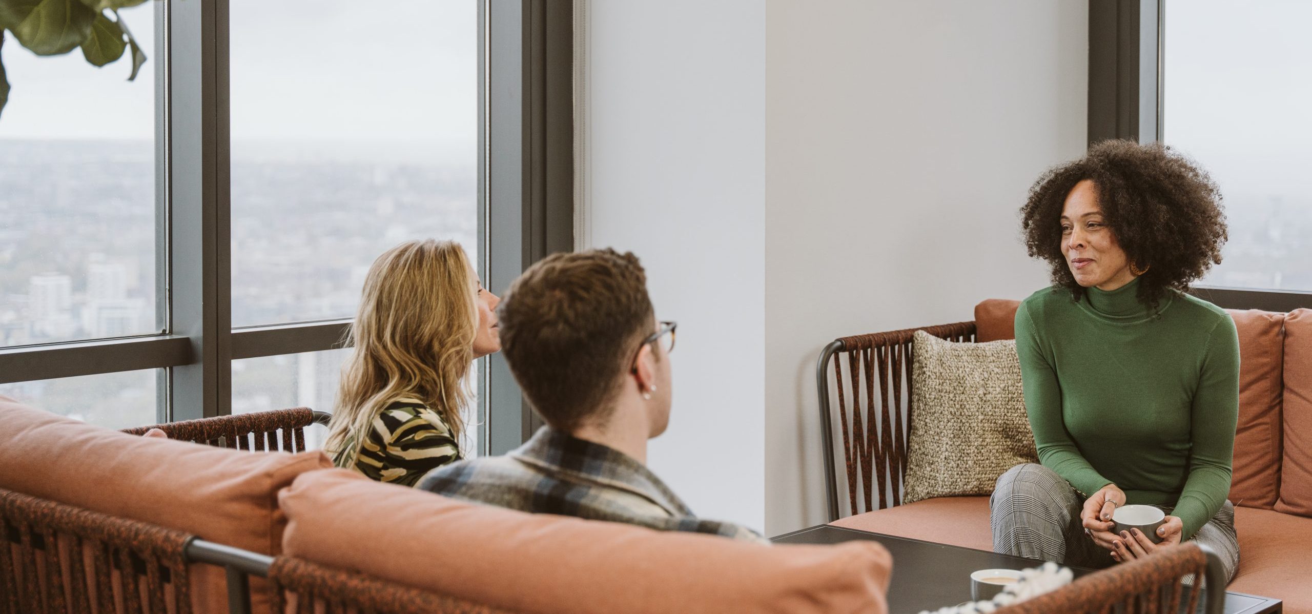 Photograph of 3 people talking around a cushioned sofa